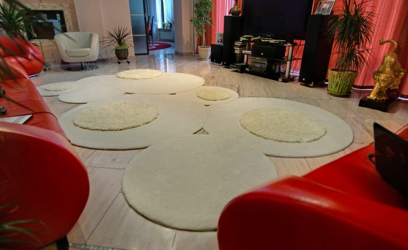 "Multi-level cream rug with round shapes on tiled floor and red couches"